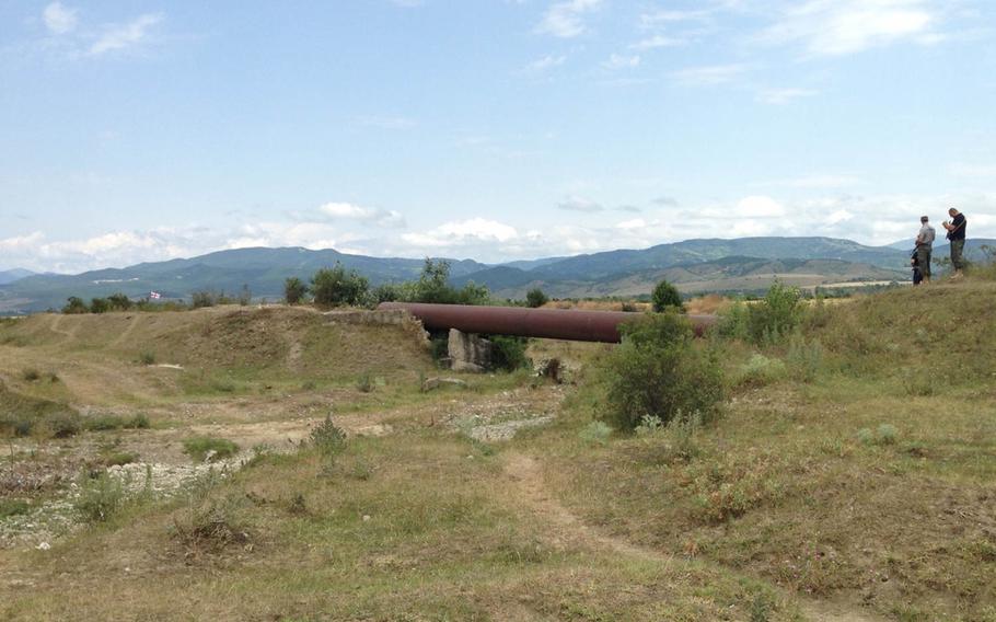 Georgian police stand on an embankment talking to armed men in uniform in the bushes at left near the boundary with the breakaway enclave of South Ossetia Thursday, July 16, 2015. Georgians took down a Russian sign and put up a Georgian flag, seen at left, earlier this week. Later Thursday, the flag was removed by a man who said he was a South Ossetian official and was accompanied by armed, uniformed men.