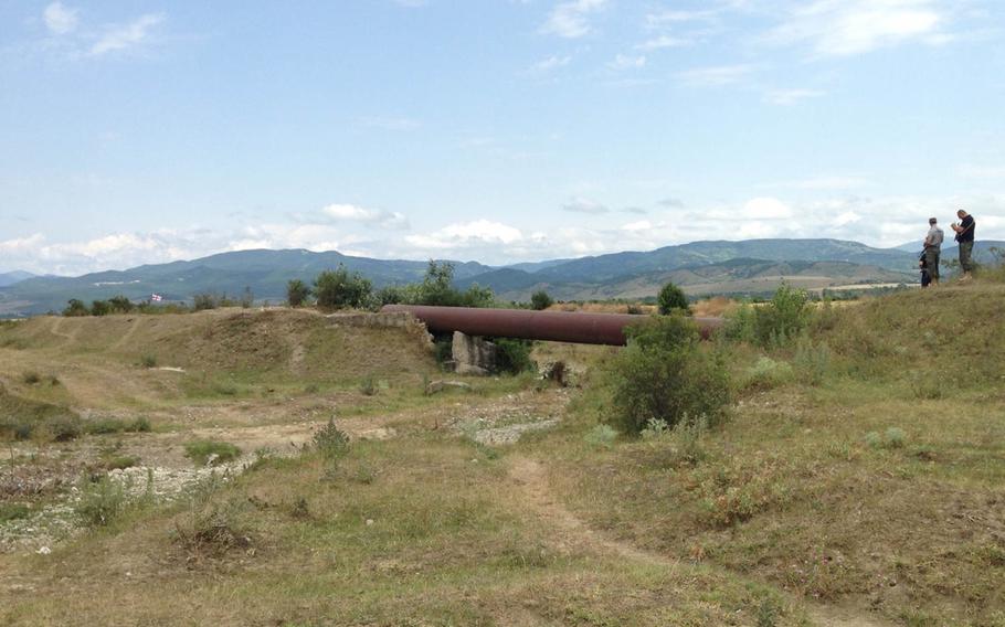 Georgian police stand on an embankment talking to armed men in uniform in the bushes at left near the boundary with the breakaway enclave of South Ossetia Thursday, July 16, 2015. Georgians took down a Russian sign and put up a Georgian flag, seen at left, earlier this week. Later Thursday, the flag was removed by a man who said he was a South Ossetian official and was accompanied by armed, uniformed men.



