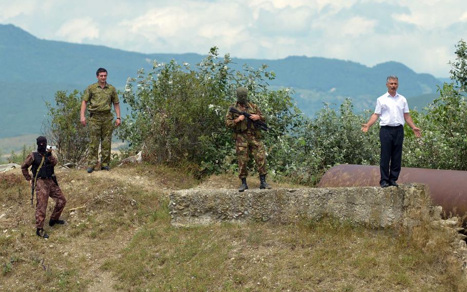 Robert Gasaev, right, who identified himself as deputy chief of the South Ossetia border control, surrounded by armed men who accompanied him, warns Georgian journalists to stay back after he removed a Georgian flag from what he said was South Ossetian territory, near Khurvaleti, Georgia, Thursday, July 16, 2015.