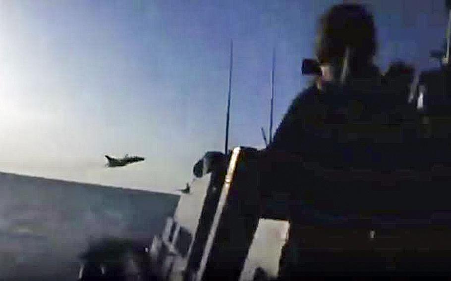 A video screen grab shows a jet passing in front of a U.S. warship.