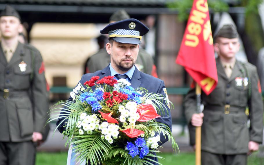 A Czech police officer carries flowers to a memorial to the American 2nd Infantry Division, during the Liberation Festival Pilsen, Friday, May 5, 2017. Behind him, re-enactors are dressed as U.S. Marines to honor the Marines who were originally part of the U.S. Army's 2nd Infantry Division.