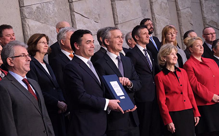 Surrounded by permanent representatives of member nations, Macedonian Foreign Minister Nikola Dimitrov, left, and NATO Secretary-General Jens Stoltenberg hold the accession protocol after signing the document at the alliance's headquarters in Brussels.