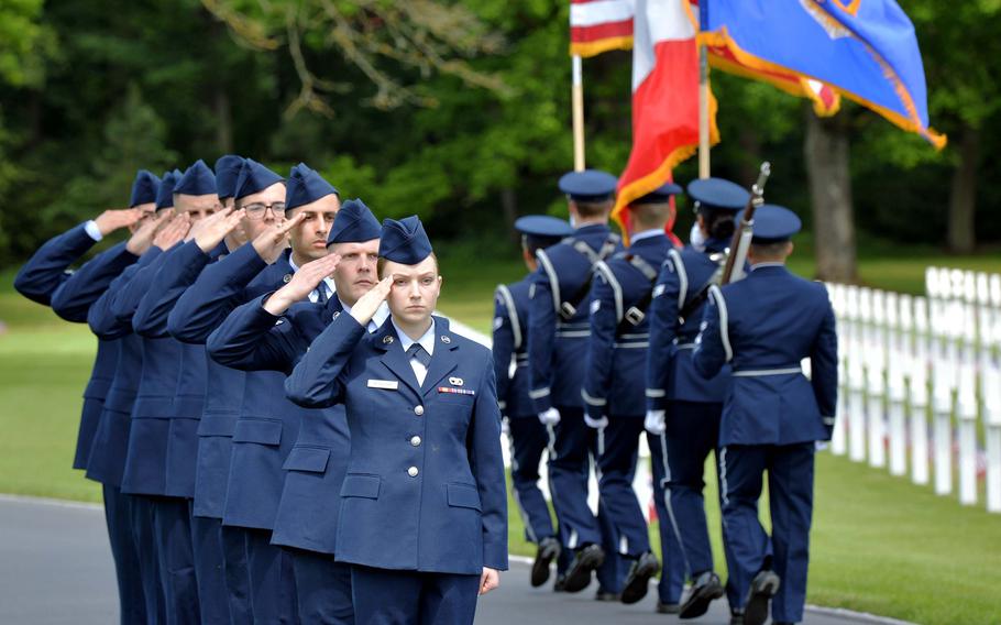 Airmen from Ramstein Air Base, who presented wreaths during the Memorial Day Ceremony at Lorraine American Cemetery, salute the color guard from the 52nd Fighter Wing out of Spangdahlem Air Base, as they march off the site at the conclusion of the ceremony.