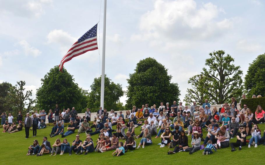 Sitting under an American flag, people watch the Memorial Day ceremony at Lorraine American Cemetery in St. Avold, France, Sunday, May 26, 2019. Around 1,500 people attended the ceremony.