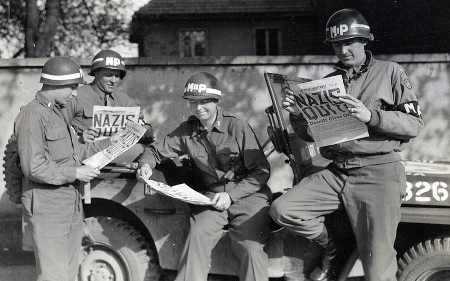 Four military policemen take a break along a German road to read in The Stars and Stripes newspaper about the Nazi surrender, ending World War II in Europe.
