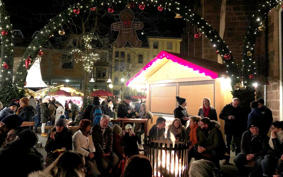A crowd sits around an open fire near the Stiftskirche in Kaiserslautern, Germany, during the 2019 Christmas market. Most Christmas markets in Germany have been canceled because of the coronavirus and large gatherings have been banned, but Germany has temporarily lifted a travel ban on Americans to allow the children of service members, Defense Department civilian employees and others covered by the Status of Forces Agreement and assigned to Germany to enter the country over the holidays.