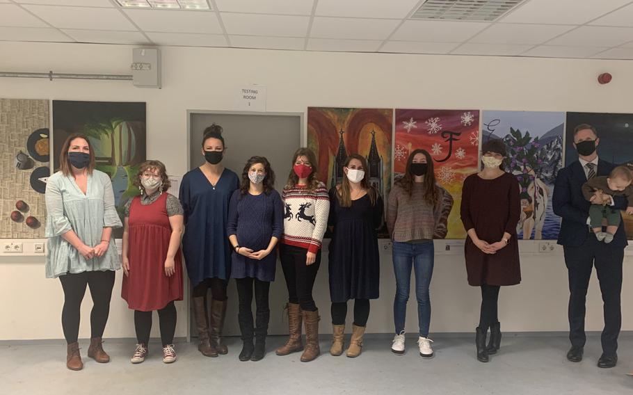 Nine artists who contributed works to an exhibtion at the acute respiratory center at Hohenfels Training Area, Germany, pose in front of their paintings on Dec. 6, 2020. The exhibition aims to take patients' minds off the discomforts of being tested for the virus.

