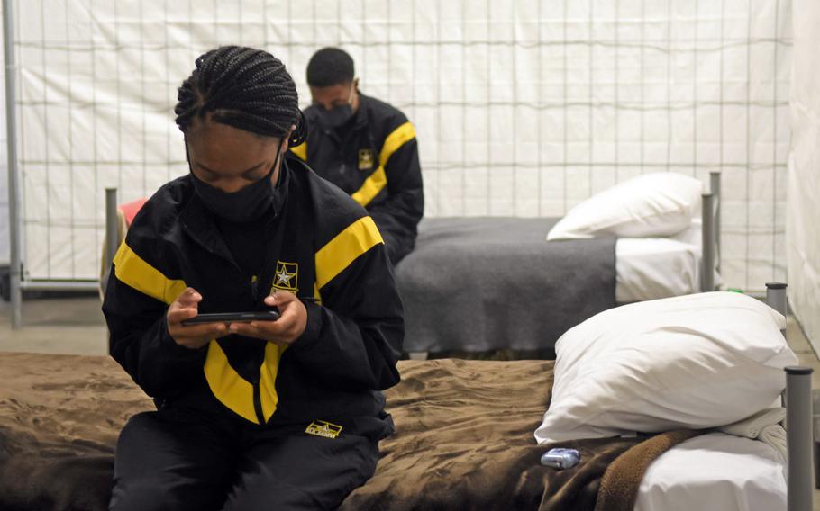 Army Pfc. Cherisse Bishop, foreground, and Sgt. Brithany Joseph check their devices while resting on their cots inside the quarantine facilities at Rhine Ordnance Barracks in Kaiserslautern, Germany, Nov. 12, 2020. Newly arriving soldiers wear Army physical training gear to make them visibly distinct from other soldiers who are further along in the quarantine process.

