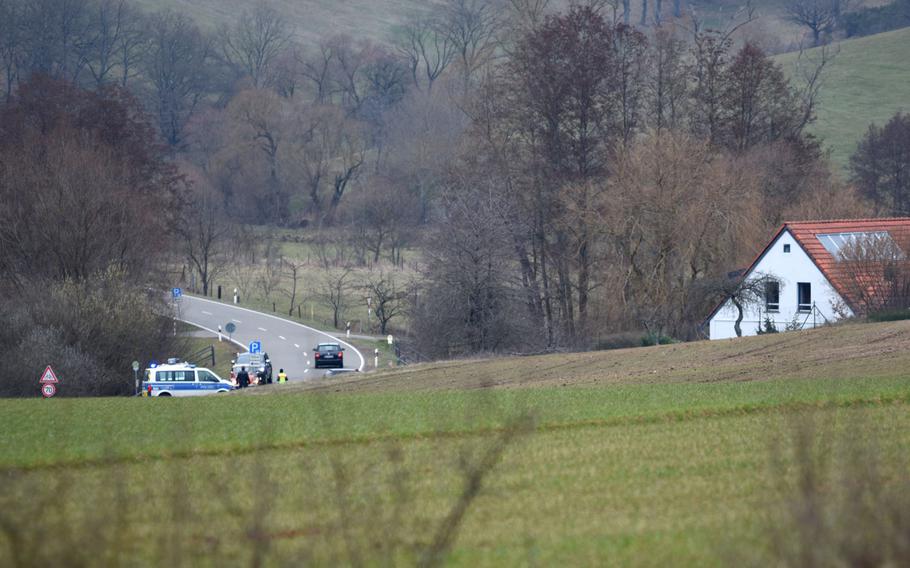 A police road block can be seen in the distance at a bend on Highway 356 between the villages of Weilerbach and Hirschhorn, Germany on Tuesday, March 9, 2021, after two people were found dead at a house in the town Tuesday. A few houses and farms are located in the blocked area.

