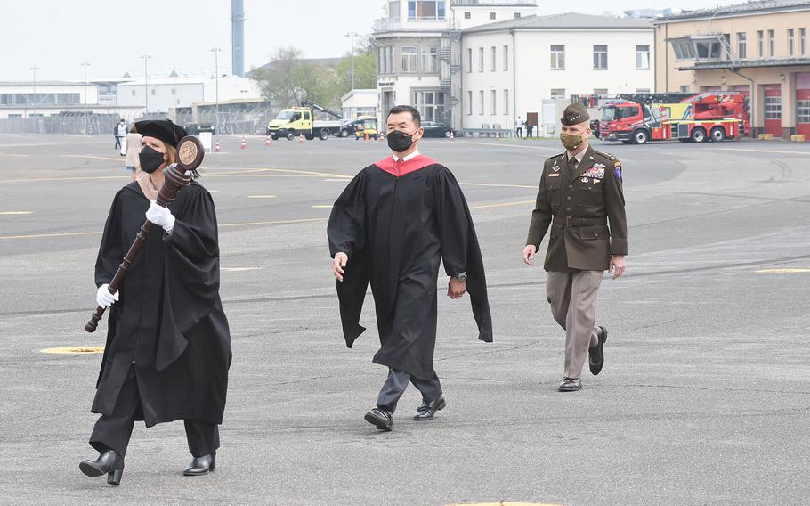 Commencement speakers for the University of Maryland Global Campus Europe class of 2021, including  Tony Cho, middle, UMGC Europe vice president and director, and Gen. Christopher Cavoli, the commander of U.S. Army Europe and Africa, walk across the airfield on Clay Kaserne in Wiesbaden, Germany, towards the stage on May 1, 2021.