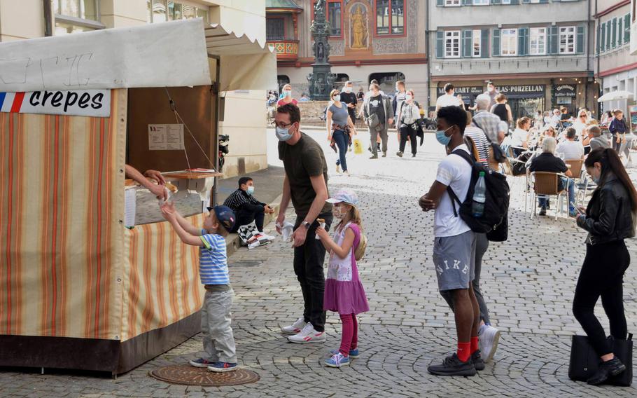 A boy is handed a crepe at a stand just off Marktplatz in Tuebingen, Germany, on March 30, 2021. German Health Minister Jens Spahn said May 7, 2021, that businesses can cautiously reopen, starting by offering outdoor dining and events, but only when new cases fall below 100 per 100,000 residents per week.
