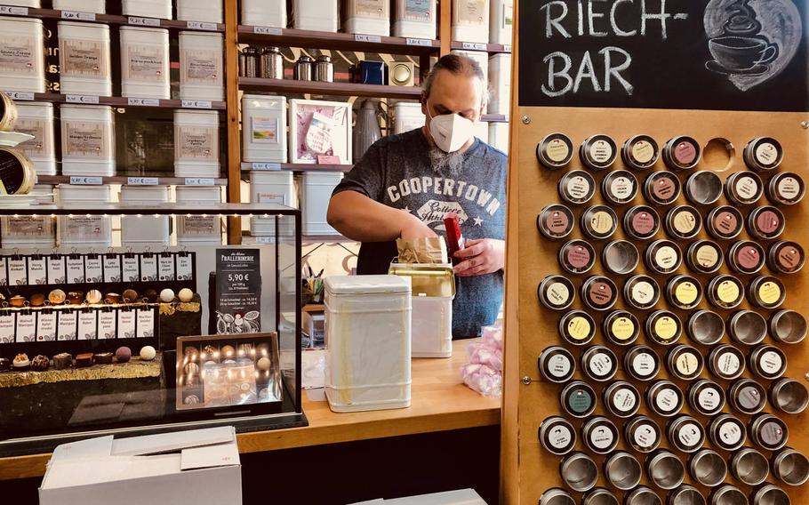 The shopkeeper at the Genussladen in Altenglan, Germany, wears a face mask as he scoops tea into a bag for a customer. German health authorities said May 7, 2021, they think the third wave of the coronavirus has been halted in Germany, but warned that it could resurge if people let down their guard.
