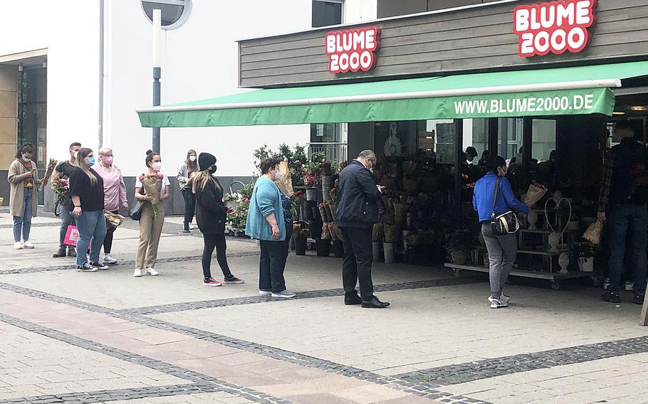 People stand in line outside a flower shop in Kaiserslautern, Germany, Saturday, May 8, 2021. Many shops in the city were closed or only allowing shopping by appointment as the city's coronavirus incidence rate remained above 100 new cases per 100,000 residents. 