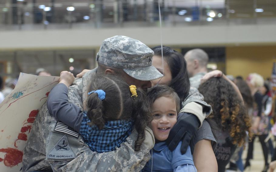 Sgt. Alexander Mason with the 146th Signal Company, embraces his family at the welcome home ceremony for the ''Old Ironsides'' advance party Tuesday night at the Wiesbaden Fitness Center.  Pictured from left to right are daughter Aminah Mason, 5; son Isaiah Mason, 2, and wife Marcia Molina.