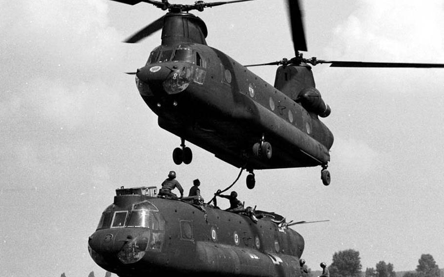 In August, 1981, a crew at Coleman Barracks in Mannheim, Germany, prepares an Army CH-47 Chinook helicopter belonging to the 205th Aviation Co. at Finthen Army Air Field for lifting by another Chinook, this one from the 295th Aviation Co. The copters were on their way to Ramstein Air Base, where the stripped-down craft from Finthen was to be loaded aboard a C-5 Galaxy for a flight to the U.S. to be rebuilt. Before the flight, the 205th&#39;s copter was reduced in weight from its normal 21,000 pounds to 11,000 by removing its fore and aft transmissions, rotors and engines.