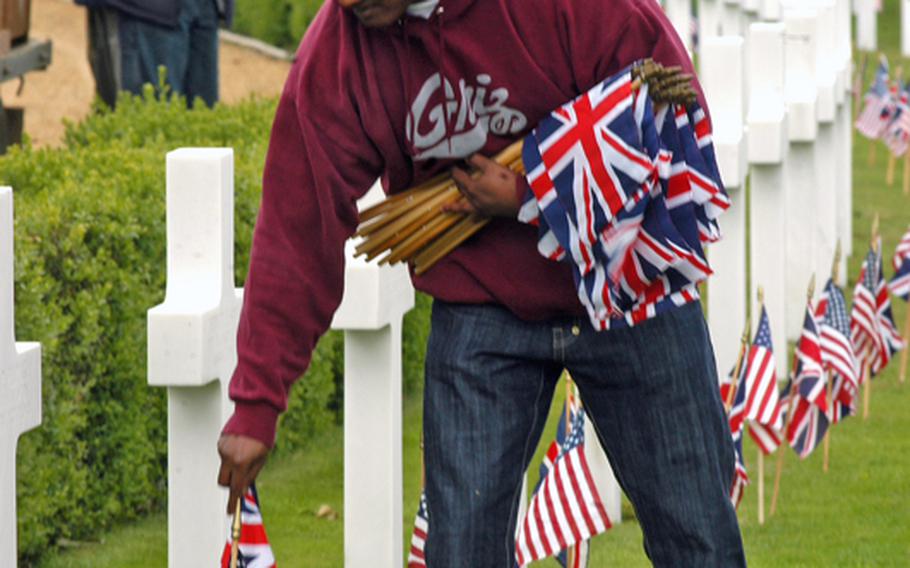 Petty Officer 2nd Class Javin Anderson places a British flag on the gravesite Friday at the Cambridge American Cemetery and Memorial. Anderson is assigned to the Defense Courier Station at RAF Mildenhall.