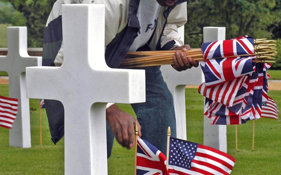 Senior Master Sgt. Haughton Morgan, of RAF Mildenhall's Defense Courier Station, places flags at the grave of a fallen U.S. servicemember at the Cambridge American Cemetery and Memorial on Friday. 