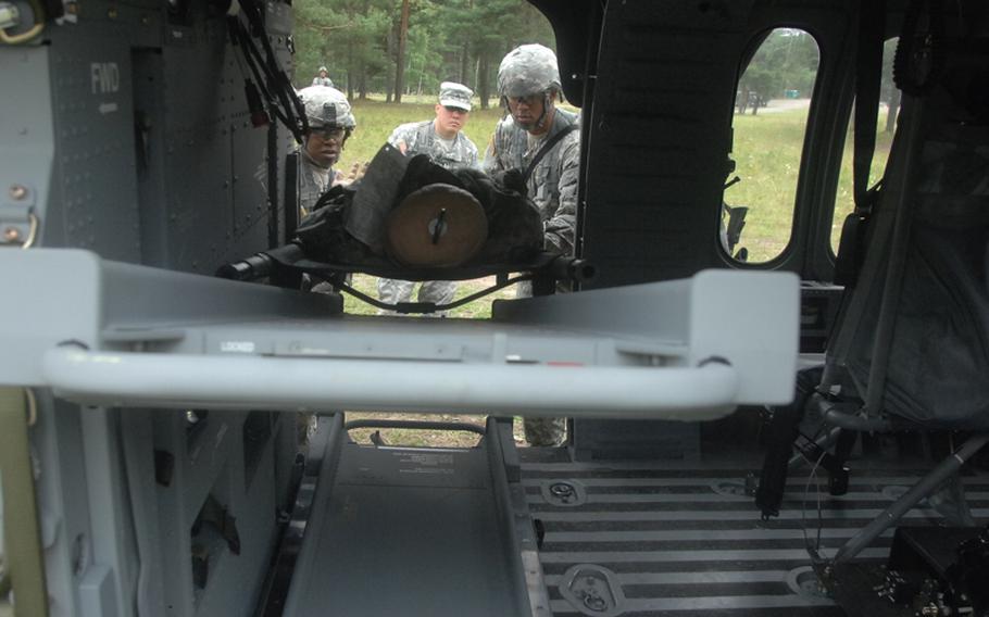 Sgt. John Rudegeair, Landstuhl Regional Medical Center, in patrol cap, watches as candidates for the Expert Field Medical Badge load a litter with a dummy into a helicopter at the Grafenwöhr Training Area. More than 300 candidates from a spectrum of medical occupations are training this week for the badge; testing begins Aug. 8.