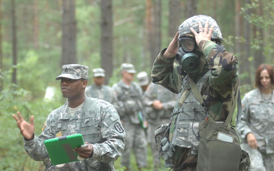 Sgt. Michael Tonjes, right, 8th Medical Logistics Company, demonstrates use of a gas mask and CBRN suit (Chemical-Biological-Radiological-Nuclear) as Staff Sgt. Timothy Miller of the 212th Combat Support Hospital describes each step to candidates for the Expert Field Medical Badge. More than 300 candidates from a spectrum of medical professions will test for the coveted badge at Grafenwöhr Training Area beginning Aug. 8.