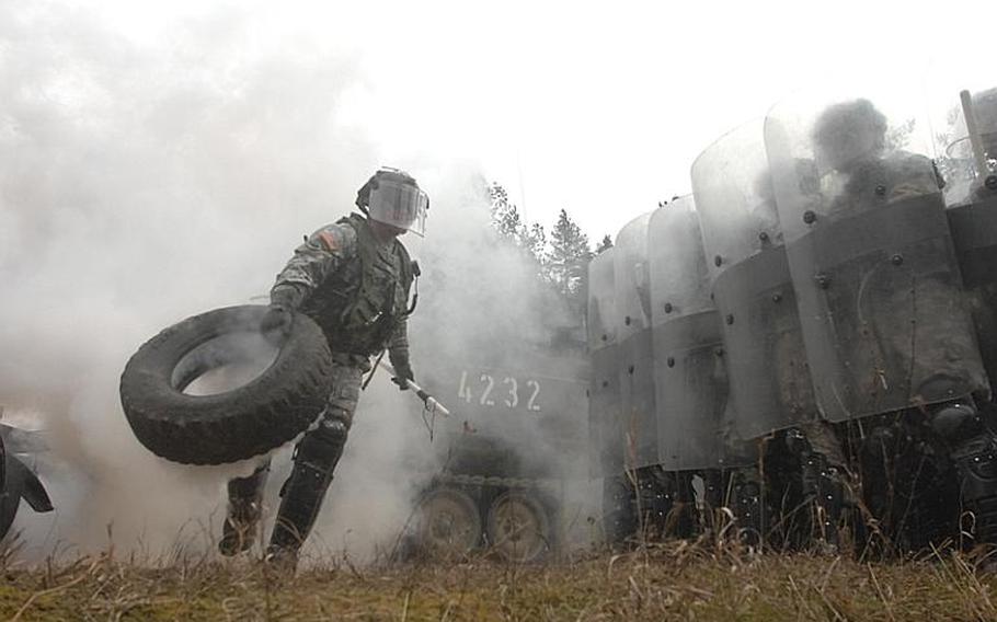 A soldier hurls a smoking tire away from the action during a civil disturbance training exercise at the Joint Multinational Readiness Center on Thursday in Hohenfels, Germany. The simulation, part of a larger exercise to train U.S. and multinational soldiers bound for peacekeeping duties in Kosovo, sought to mimic recent events in the country.