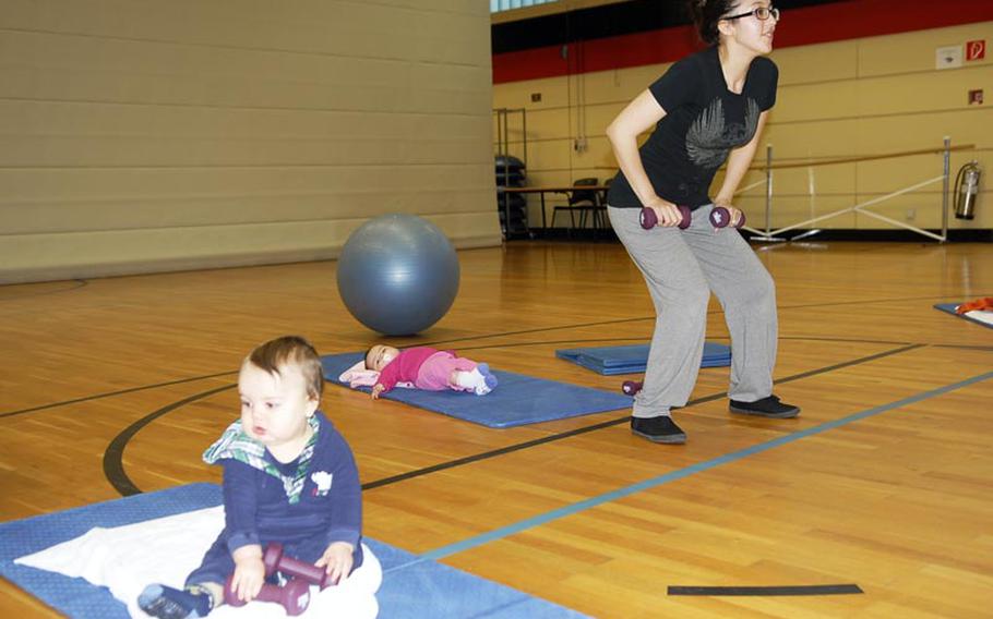 Melissa Van Hausen lifts weights while her baby daughter lies on a mat behind her and another baby plays with some weights during a recent Binkies and Babes class at the Landstuhl Regional Medical Center fitness center.