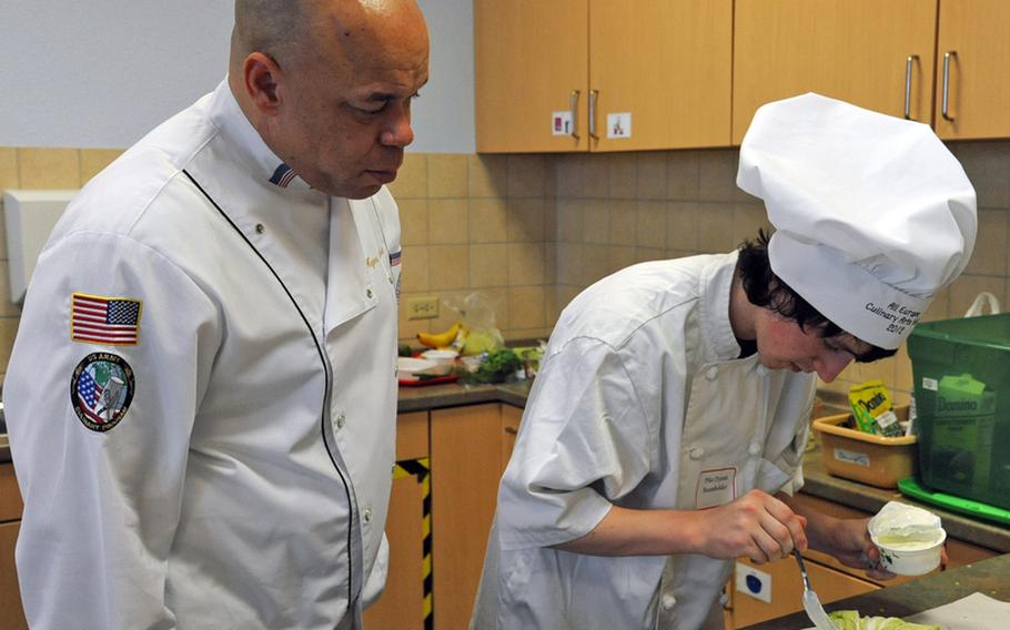 Master Sgt. Major Luckett, a judge for the cooking competition at the DODDS-Europe Culinary Arts Faire, watches Baumholder&#39;s Dyami Pike put finishing touches on his team&#39;s appetizer, cabbage leaves stuffed with pork and couscous.
