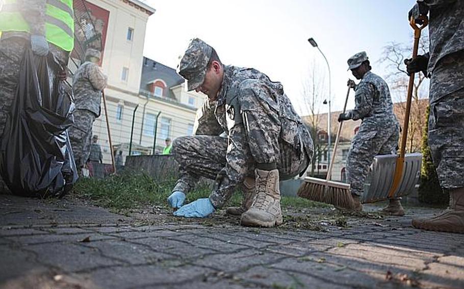 Soldiers with the 266th Financial Management Center in Kaiserslautern, Germany, remove grass and debris from the sidewalk Thursday, April 25, 2013, outside Kleber Kaserne. Soldiers around Europe spent the morning cleaning up bases as part of community spring cleanups.