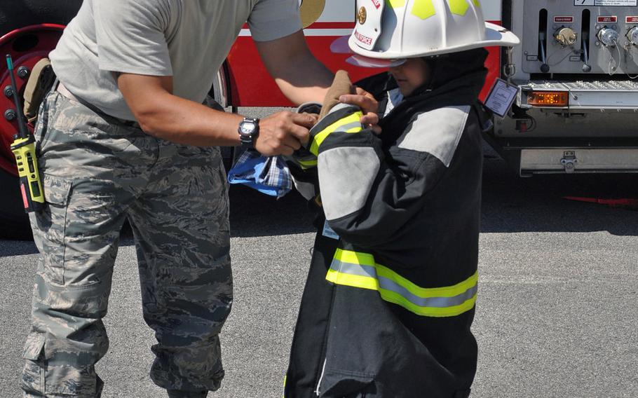 Master Sgt. Angus Adolpho, Aviano assistant fire chief, helps a visitor try on a fire suit during a tour of Aviano Air Base's fire department, Friday, July 10, 2015.