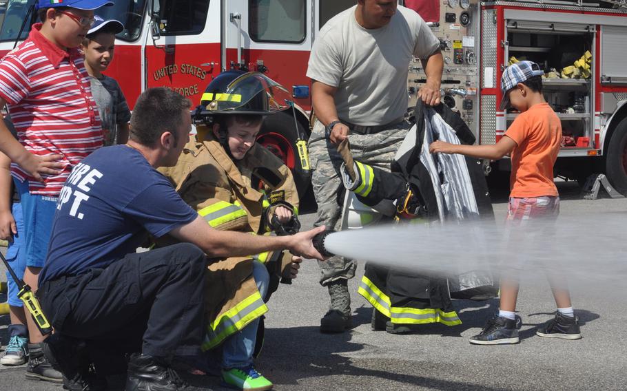 Mateo Copetti, an Italian fire fighter at Aviano Air Base, assists a young visitor sprayer water from a fire engine's hose Friday, July 10, 2015, during a tour of the base in Italy.
