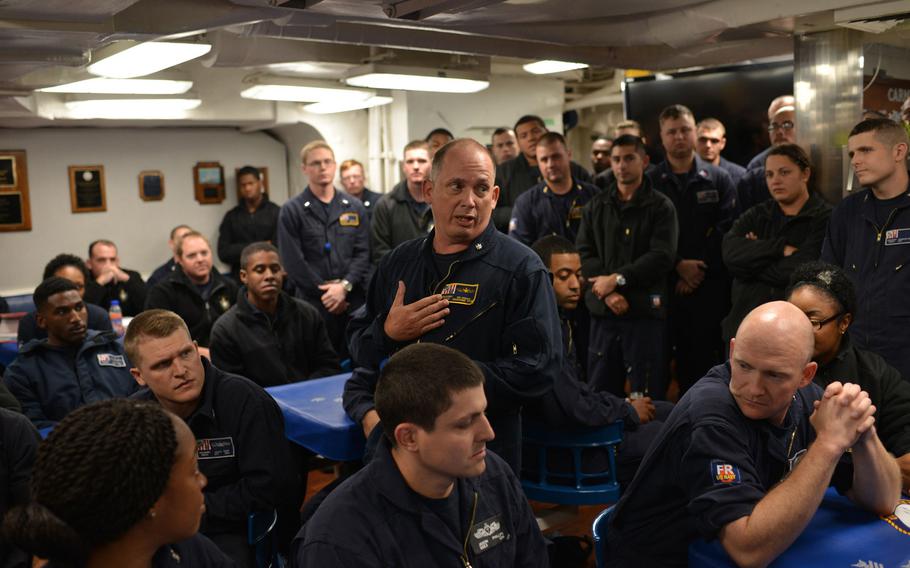 Cmdr. Ken Pickard, commanding officer of the guided-missile destroyer USS Carney, speaks to crewmembers in the mess hall Sept. 23, 2015. Pickard is wearing 'flyers coveralls,' 1 of 2 new flame-resistant sets of coveralls being tested by the Navy aboard the Carney. Several sailors behind Pickard can be seen wearing traditional utility coveralls.