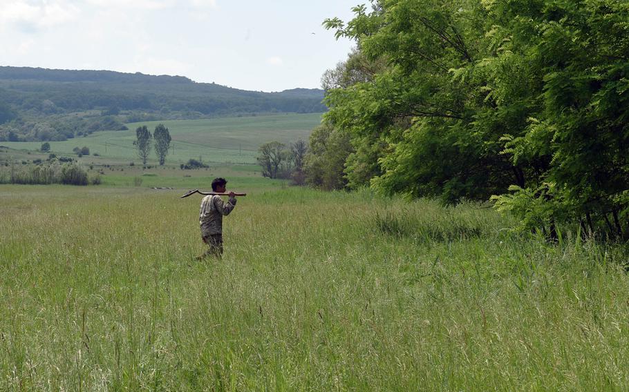 A soldier with the Army's 2nd Cavalry Regiment walks across a grassy field with a shovel to dig a fighting position, in Cincu, Romania, Monday, June 17, 2019.