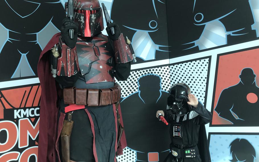 Logan Hinton, 31, dressed as a Mandalorian from the ''Star Wars'' galaxy and son Silas, 4, dressed as Darth Vader, pose together in front of a KMCC Comic Con backdrop during an event for comic book and other costumed fans at the Ramstein main exchange on Sunday, Sept.22, 2019.