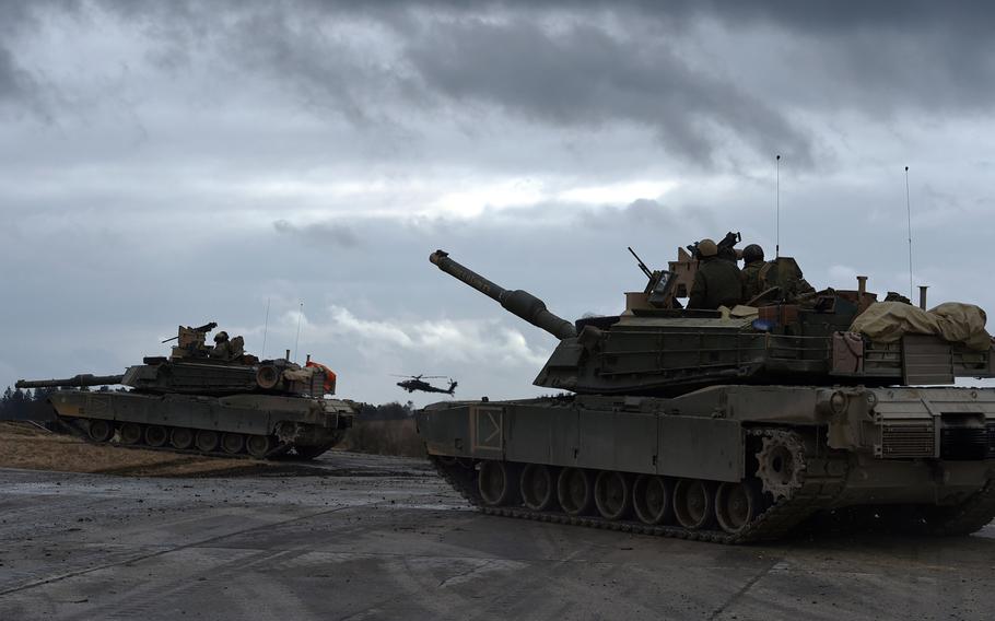 U.S. Army M1A2 Abrams tanks and an AH-64 Apache helicopter are ready to attack an enemy position during a live-fire exercise at Grafenwoehr, Germany in 2018. The Army will deploy a division headquarters, three tank brigades and scores of other troops to Europe early next year for what will be the largest American-led war game on the Continent in 25 years, U.S. European Command said Monday, Oct. 7, 2019.