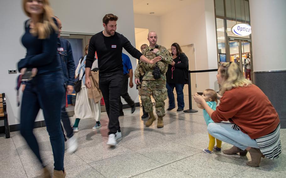 John Krasinski, from the Amazon series ''Jack Ryan,'' waves at a baby as he walks through the base exchange during a USO visit to Ramstein Air Base, Germany, Oct. 15, 2019.