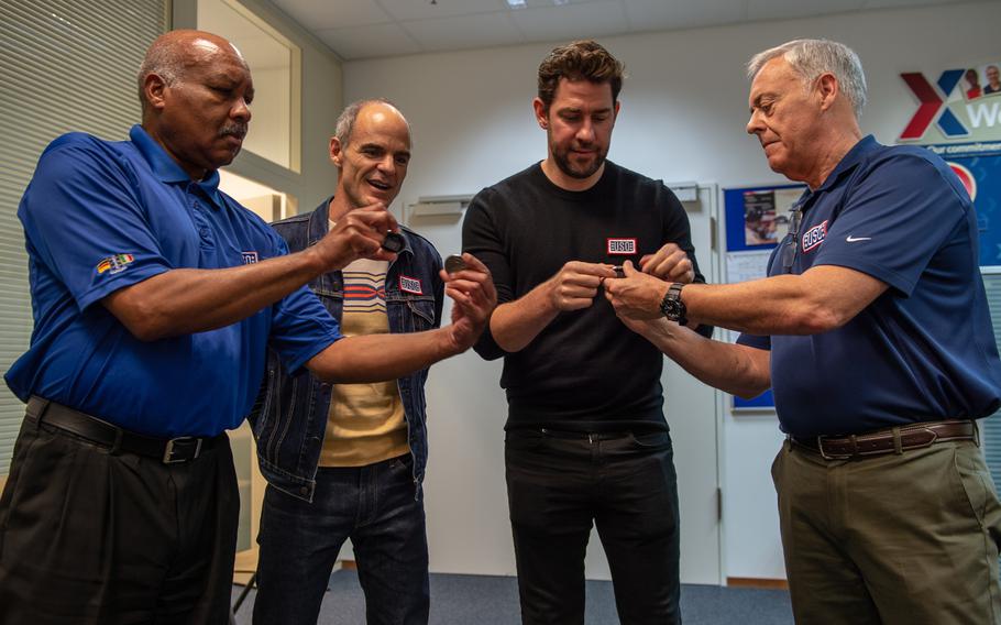 Mike Lewis, left, regional director of operations for USO Europe, shows the first ever Bob Hope coin to Michael Kelly as John Krasinski looks at the coin he received from Regional Vice President Walt Murren.