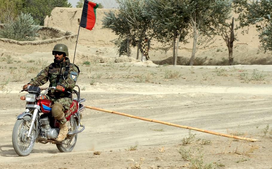 An Afghan soldier drags a rake behind a motorcycle to search for roadside bombs in Zabul province.