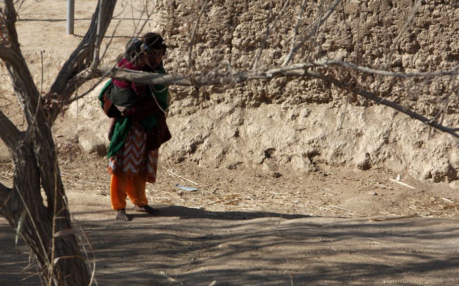 An Afghan child holding an infant watches a passing convoy (not shown) conducted by 8th Engineer Support Battalion, 1st Marine Logistics Group (Forward), through a village in Marjah District, Helmand province, Afghanistan, Jan. 11, 2011.