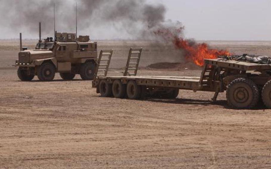 Smoke from an active burn pit at Camp Leatherneck, Afghanistan, drifts towards an MRAP vehicle June 25, 2011.