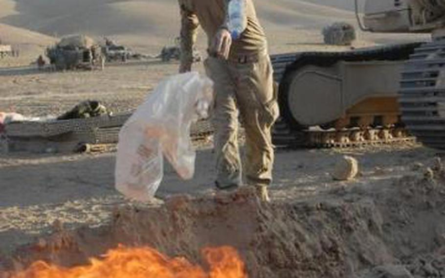 A soldier with the 24th Infantry Regiment tosses trash into a burn pit outside a checkpoint in the Zabul province of Afghanistan, Sept. 14, 2011.