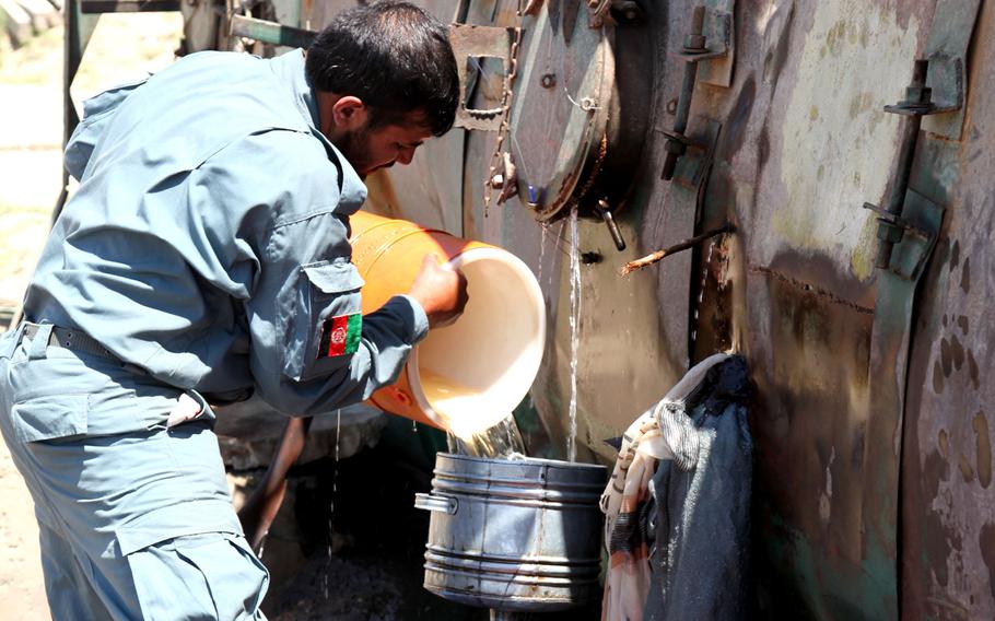 An Afghan National Policeman pours gasoline leaking from a fuel truck into barrels for the local people in Logar province, Afghanistan in this June 2010 photo.