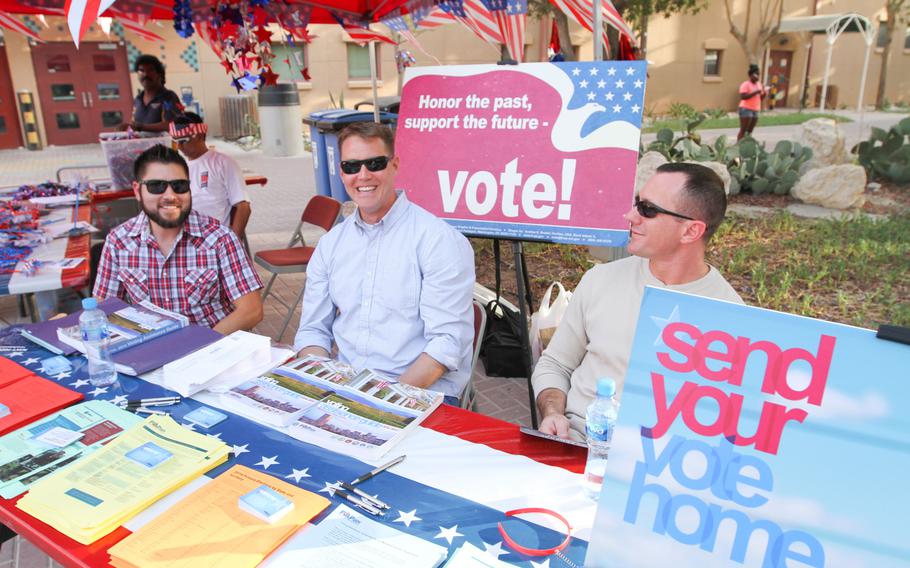 Army Staff Sgt. Aaron Reeder, on the right, Lt. j.g. Heath Hilleshiem, in the middle, and David Buitrago, on the left, pass out information on voting at the ''Freedom Rocks'' celebration, put on by Morale, Welfare and Recreation at Naval Support Activity Bahrain, on July 3, 2014.