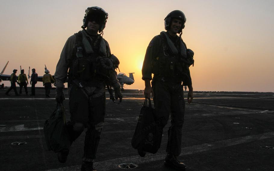 Two Naval aviators walk across the flight deck of the USS George H.W. Bush, underway in the Persian Gulf, after completing a flight, Aug 10, 2014. F/A 18s are among launched from the Bush are among aircraft  conducting air strikes in Iraq.
