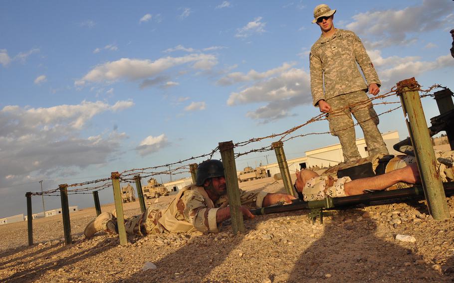 Sgt. William Winstead watches Iraqi soldiers crawl under barbed wire while hauling a soldier, playing an injury victim, on a litter at Camp Fallujah, Iraq, on Jan. 19, 2010. The Iraqi soldiers were participating in a timed obstacle course as part of their training in combat first aid. 
