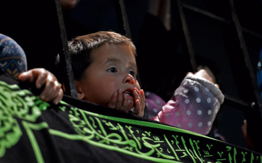 An Afghan child watches as men flagellate themselves at a Muharram ceremony on the day of Ashoura in Kabul. Women and children watched from upper levels as the men cut their backs with knives and chains.