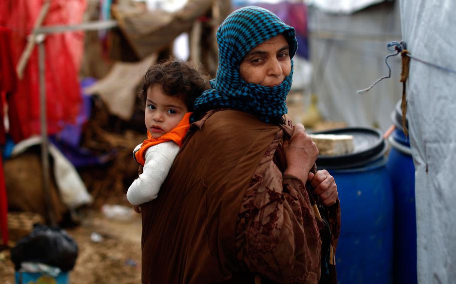 In this Monday, Jan. 4, 2016, file photo, a Syrian refugee carries a baby on her back at a refugee camp in the town of Hosh Hareem, in the Bekaa valley, east Lebanon. In a report published Tuesday, Jan. 12, 2016, the New York-based rights group Human Rights Watch said Lebanese residency laws are putting Syrian refugees in danger. The regulations, adopted a year ago, have forced refugees to either return to Syria, where they are at risk of persecution, torture or death, or to stay in Lebanon illegally, leaving them vulnerable to exploitation and abuse.