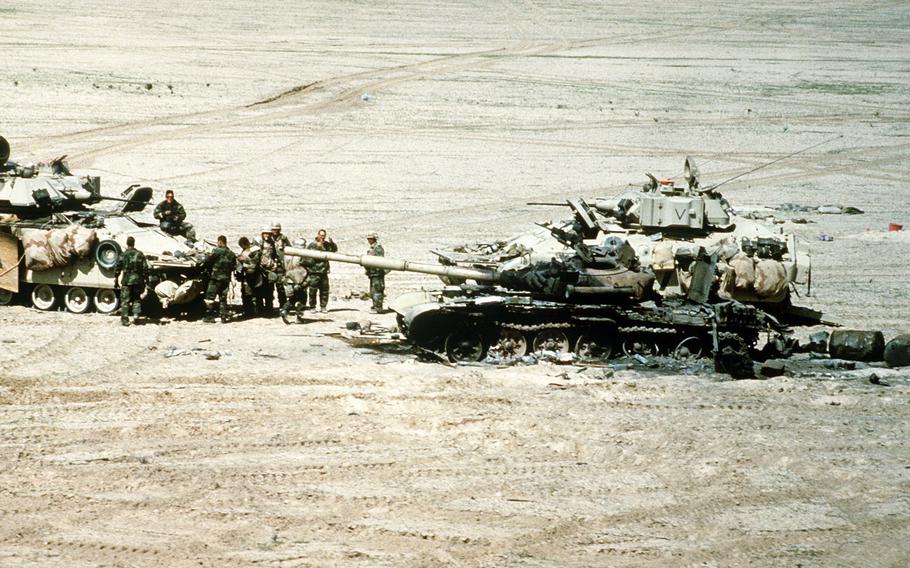 U.S. military personnel gather near a demolished Iraqi T-72 main battle tank, destroyed by allied forces during the Gulf War, March 3, 1991.  M-2 Bradley vehicles are parked near the tank. 


