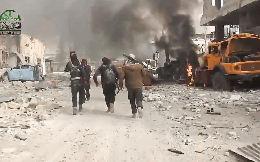 A screen grab from a video posted on Tuesday March 21, 2017, shows fighters from the Ahrar al-Sham militant group running past a buring truck during a battle against the Syrian government forces, in an eastern neighborhood of Damascus, Syria.