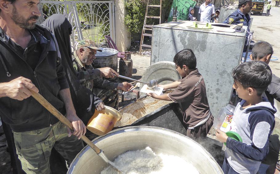Shiite volunteers help feed children in a liberated neighborhood of west Mosul, near the Old City, where Iraqi security forces continue to battle Islamic State militants who have held the city for nearly three years.