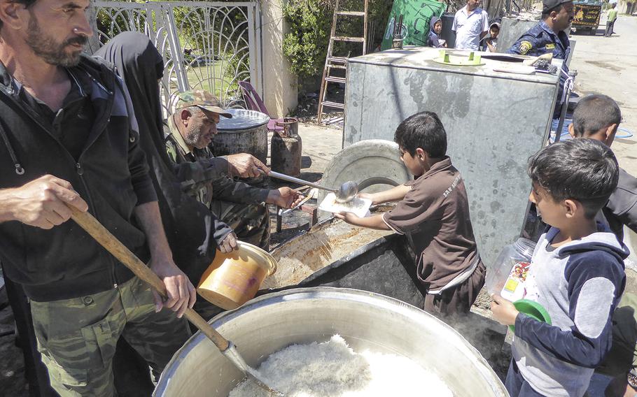 Shiite volunteers help feed children in a liberated neighborhood of west Mosul, near the Old City, where Iraqi security forces continue to battle Islamic State militants who have held the city for nearly three years. 