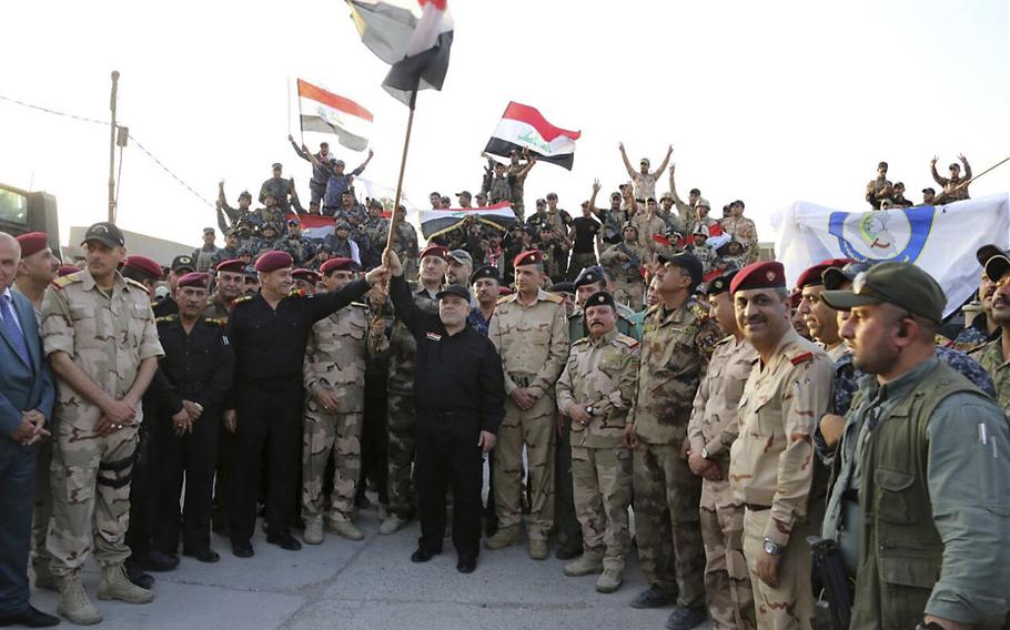 Iraq's prime minister Haider al-Abadi raises the national flag as he addresses forces from a small base on the edge of Mosul's Old City, where heavy clashes have been underway for days, Monday, July 10, 2017. Al-Abadi returned to Mosul Monday and declared victory against the Islamic State group in the northern city following nine months of grueling urban combat.